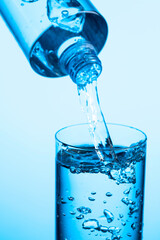 Pouring water from a bottle into glass on a blue background.