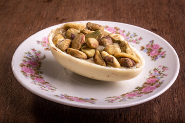 Mini stuffed white chocolate with pistachio easter egg on a white plate with flower design on a wooden table.