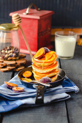 pancakes with a sweet plum and honey in a frying pan on a blue wooden background. a glass of milk. rustic style