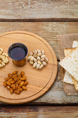 Matzah on sacking and a round board with nuts and a glass of wine for kiddush on a wooden table.