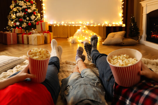 Family with popcorn watching movie on projection screen in room decorated for Christmas, closeup. Home TV equipment