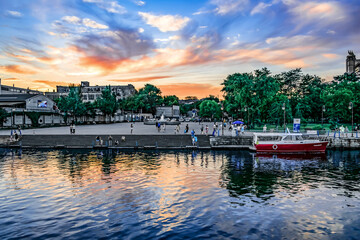 Fototapeta premium Kherson, Ukraine - July 22, 2020: View from the Dnieper River to the Kherson promenade on a summer evening. Evening cityscape with beautiful pink and blue sky reflected in the water