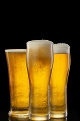 Three refreshing and cold glasses of beer isolated over black background in a studio shot