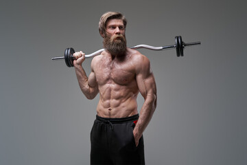 Fitness man poses in gray background holding barbell on his shoulder