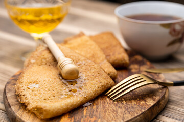 Pancakes with honey and tea on a wooden tray. gold knife and fork.