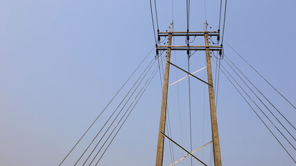 Fototapeta premium High-voltage lines on poles. Double concrete poles with power transmission line and guy wire for the tension of the electric poles on a clear sky background with copy space. Selective focus