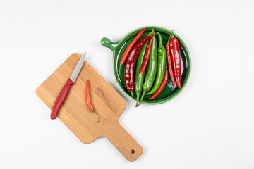 Green and red hot chilli peppers on green plate, red  pepper on a wooden board with knife, white background, chopping board, flat lay. Seasoning