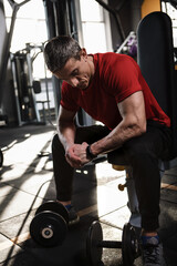 Vertical shot of a muscular sportsman resting while exercising with heavy dumbbells at the gym