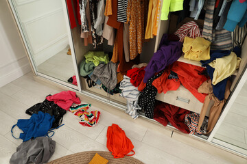 Messy wardrobe with different clothes indoors. Fast fashion concept