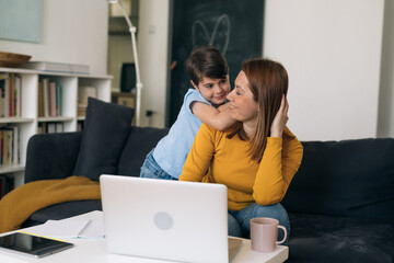 mother working from home. her son giving her support by hugging her