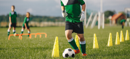 Kid soccer player dribbling through cones. Boy in soccer uniform practice with ball. Child kicking...