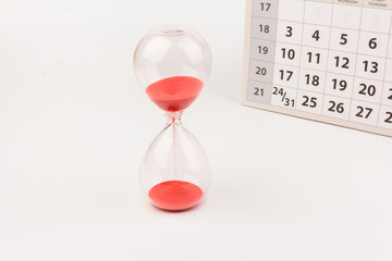 Time passing concept. Crystal hourglass with red sand and calendar on light background