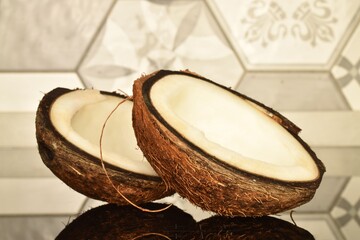 Two half of a ripe coconut, close-up, on a background of tiles.