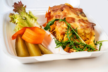Baked pasta with salad, carrot and cucumber in food box.
