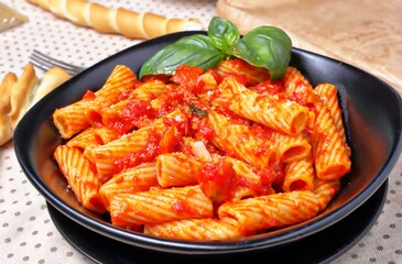 Gustoso piatto di pasta italiana condita con sugo di pomodoro e basilico disposto su un tavolo apparecchiato per il pranzo.