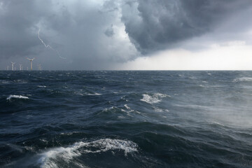 Ein Offshore Windpark mit aufgewühlter See in einem Sturm mit Blitz - obrazy, fototapety, plakaty