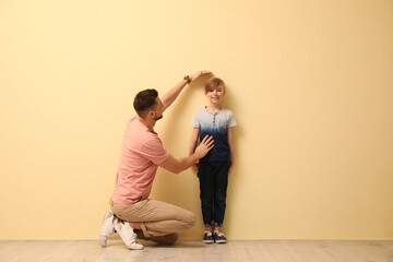 Father measuring height of his son near beige wall indoors - Powered by Adobe