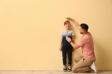 Father measuring height of his son near beige wall indoors. Space for text