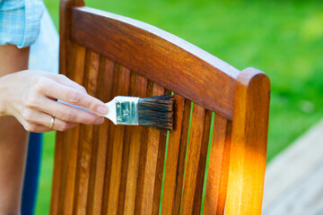 female hand holding a brush applying varnish paint on a wooden garden chair- painting and caring for wood - 420832464