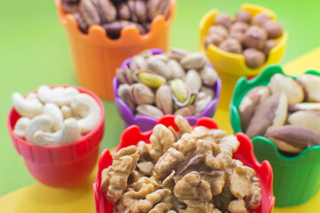 Nuts for children in colorful cups. Walnuts, pistachio, hazelnuts, brazil nuts, cashews, pecans. Healthy food, useful microelements and vitamins. Useful snack. Selective Focus