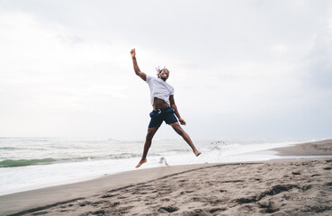 Happy young ethnic man jumping on sandy beach
