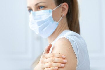 Woman with blue eyes in white T-shirt wearing protective medical mask getting ready to be vaccinated. Covid-19 vaccination campaign. Focus on hand. White background.