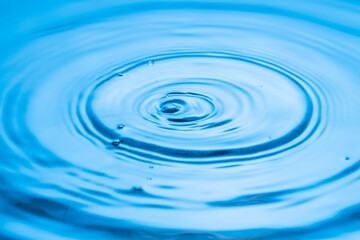 View macro of drops making circles on blue water surface isolated on background.