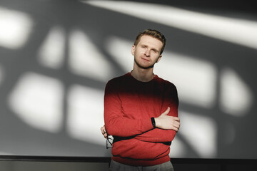 Young man in a red sweater on a white background with shadows from the light. Copy, empty space for text