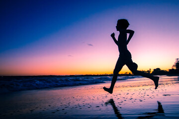 Plakat Silhueta de uma criança correndo em direção ao mar durante lusco fusco do pôr do sol em uma praia.