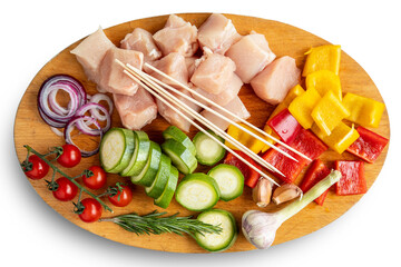 Chicken pieces, cherry tomatoes, zucchini, paprika, onion, garlic, rosemary, skewers on a cutting board. White background.
