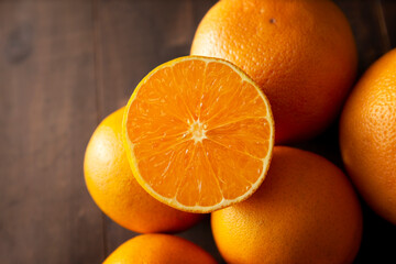 close up of a ripe orange cut in half and several whole oranges on brown rustic wooden table with copy space