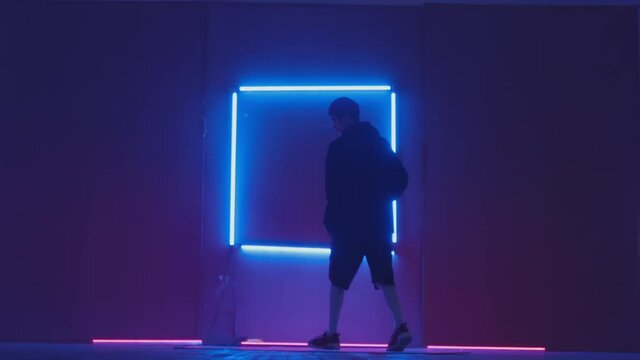 Person in windbreaker and red cap dancing to breakdance. blue rectangle neon background . Flickering neon background . man dancing to breakdance in night club