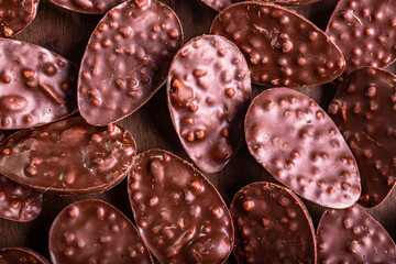 Top view of lots of mini crunchy stuffed chocolate easter eggs on a wooden table.