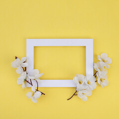 White frame with flowers on a yellow background. Flower composition. Minimal creative concept.Copy space Template for postcard, invitation, lettering text or your design