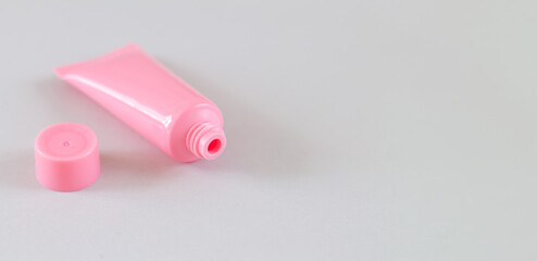 Open pink cosmetic tube on gray background