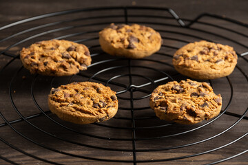Top view of chocolate chip cookies on black rack, with selective focus, on wooden table, horizontal