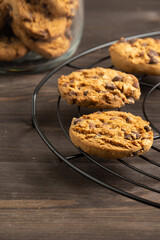Top view of chocolate cookies on black rack and glass jar, with selective focus, on wooden table, in vertical