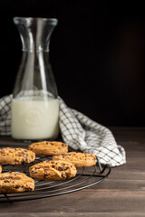 View of chocolate cookies on rack, bottle with milk and cloth, selective focus, on wooden table, and black background, vertical, with copy space
