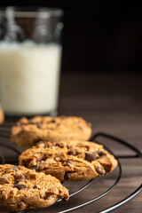 Close-up of chocolate cookies on wire rack, glass of milk, selective focus, on wooden table, vertical, with copy space