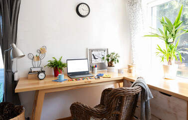 Office room with wooden office desk, window with plant, chair and laptop with empty screen. White wall with clock at home. Creative palce for work. Business.