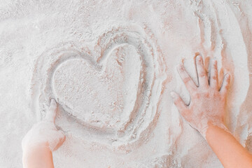 The hand of a young girl draws a heart on the white beach sand close-up. Symbol or sign of love concept