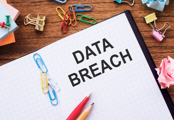 Notepad with the text DATA BREACH on the table with colored paper clips and crumpled sheets.