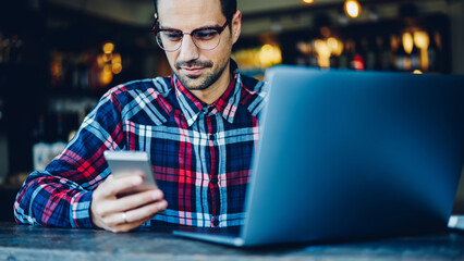 Skilled freelance copywriter working remotely at modern netbook computer while reading received sms...