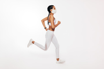 Fototapeta na wymiar Side view of young fitness woman running over white background wearing a face mask