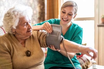 Female caretaker measuring senior woman's blood pressure at home
