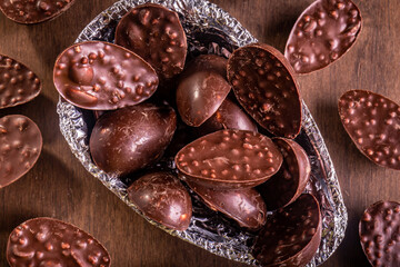 Top view of a close up of mini stuffed chocolate easter eggs inside of a half of an easter egg wrapped in an aluminium paper. Some mini stuffed easter eggs around it on a wooden table.