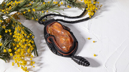 Black leather pendant amulet with orange amber on a white surface. Traditional Slavic culture,...