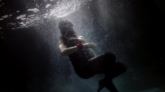mysterious brunette dressed masquerade mask and corset is whirling underwater in dark pool