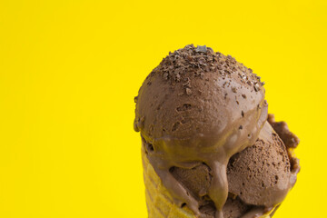 Close-up on chocolate ice cream in a waffle cone on the yellow  background. Copy space.