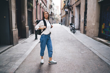 Beautiful female backpacker visiting ancient town during spring solo vacations looking around in quarter, Caucasian woman dressed in casual clothing recreating during international holidays